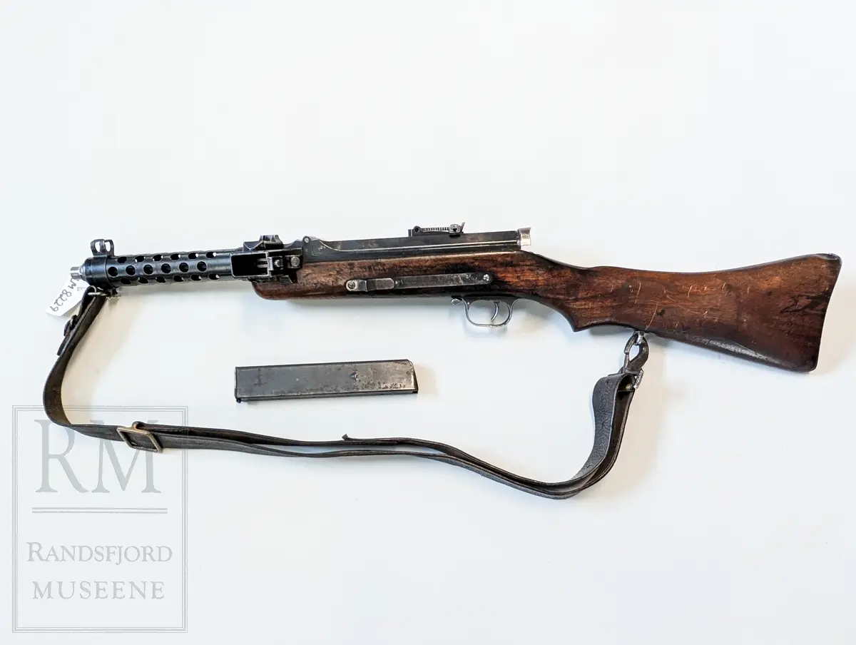 Maskinpistol .Kaliber 9 mm. Parabellum. Magasin: 33 skudd. Munningshastighet 418m/s