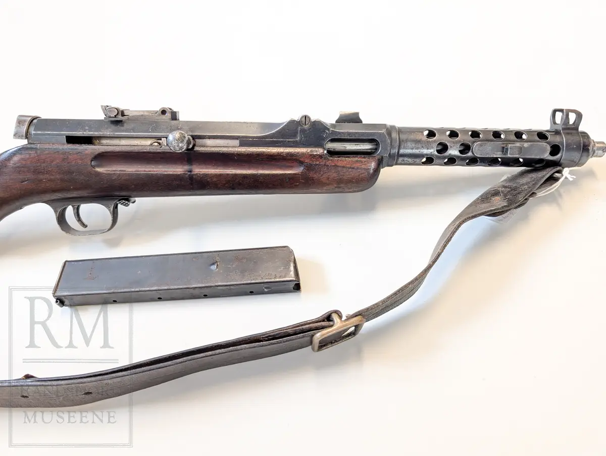 Maskinpistol .Kaliber 9 mm. Parabellum. Magasin: 33 skudd. Munningshastighet 418m/s