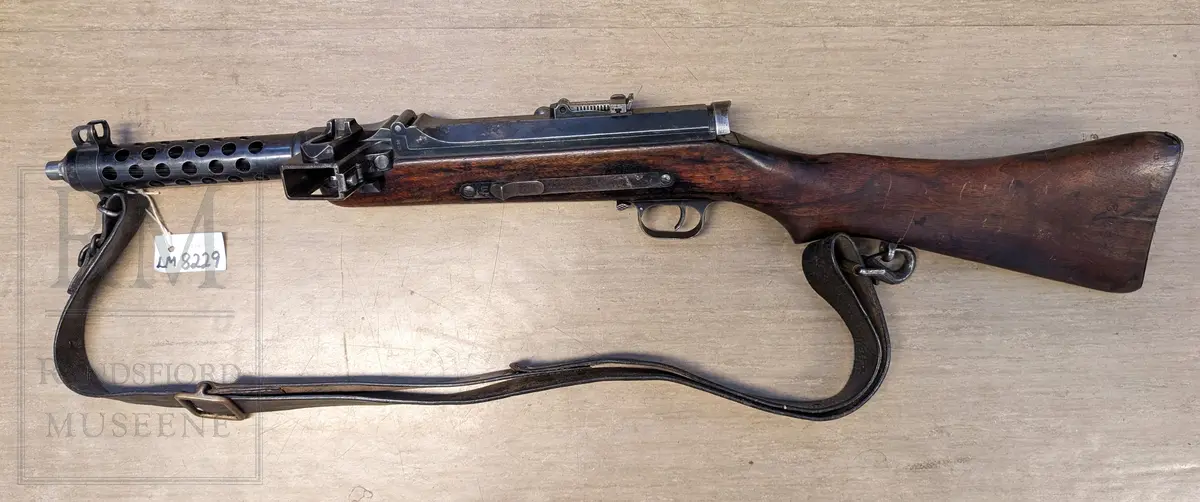 Maskinpistol .Kaliber 9 mm. Parabellum. Magasin: 33 skudd. Munningshastighet 418m/s