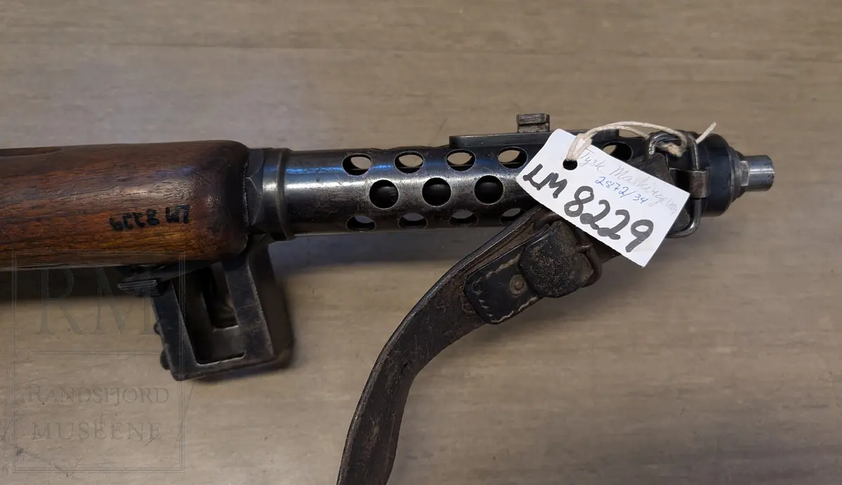 Maskinpistol .Kaliber 9 mm. Parabellum. Magasin: 33 skudd. Munningshastighet 418m/s