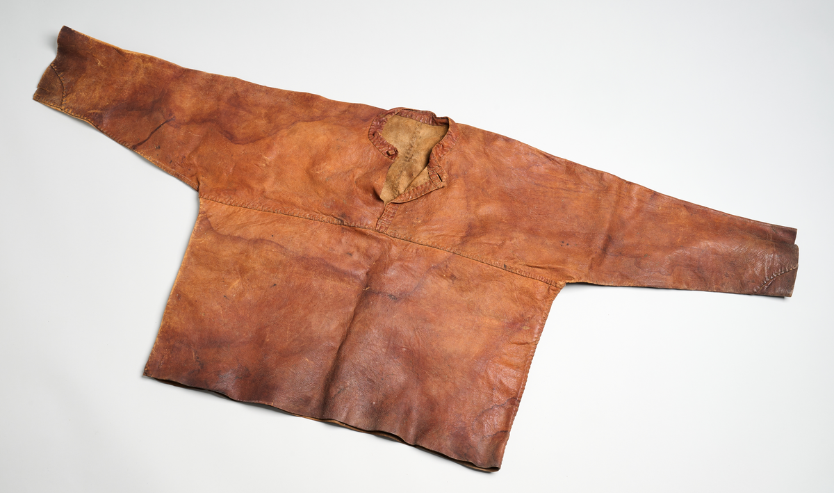 Skinntrøye med rund hals og åpning midt foran med stolpe. Knapp av sammenrullet skinn for lukking i halsen med et knapphull.  Ermene er ikke isydd ved skuldrene. De er helklipt fram til midt foran og midt bak. Sammensydd midt bak. Dette fungerer som bærestykke. Bolen er sydd sammen i sidene.
Alt er sydd med dobbelsøm med smale skinnsnorer. Smal krage/linning. Rett avskåret ved nedre kant og ermer. Skinnet er skjøtet på med små biter på ermenes nedre kant, under høyre erme bak og i høyre side nedre kant bak. To smale, lange skinnremser er sydd fast i sømmen på venstre side i ryggen. Skinnet er stivt.