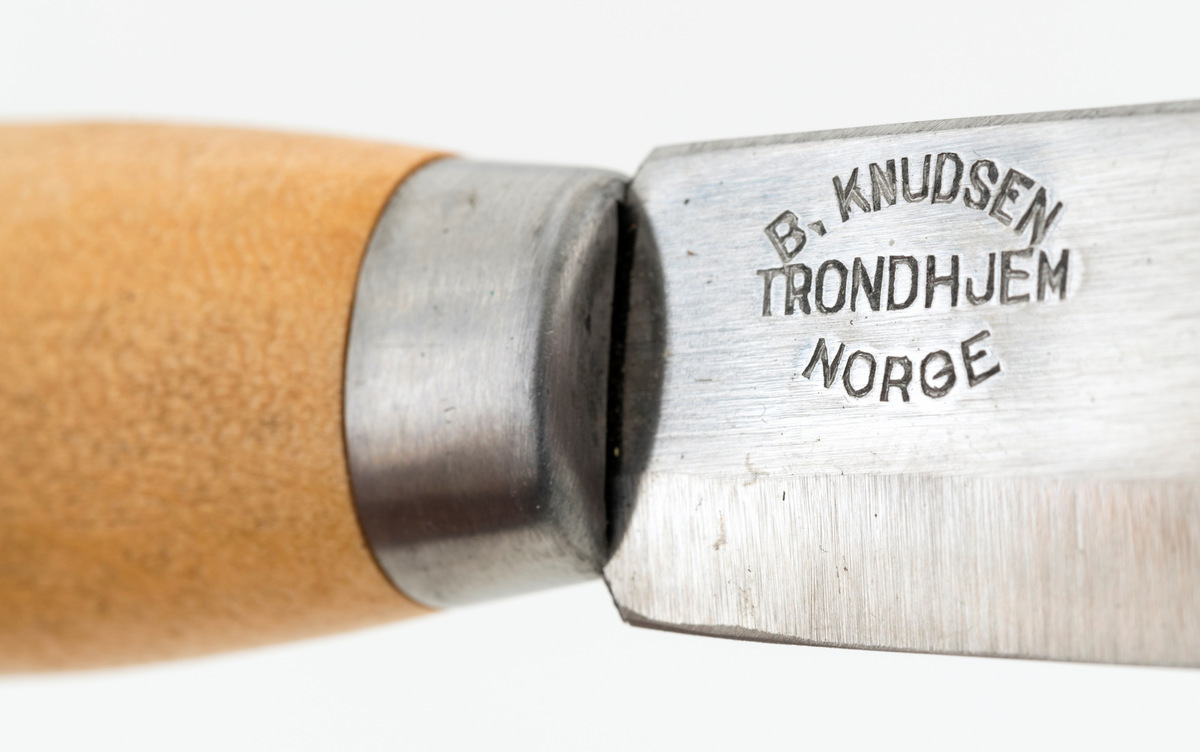 Tollekniv med slire. Denne kniven er fabrikkprodsert, og bladet minner om de populære svenske Mora-knivene, men er stemplet «B. KNUDSEN  TRONDHJEM  NORGE». Denne produsenten skal ha holdt det gående fra tidlig i 1890-åra til tidlig på 1960-tallet, med to generasjoner ledere - se fanene «Historikk» og «Opplysninger».

Kniven er 20,9 centimeter lang, målt fra bladspissen til den bakre enden av skaftet. Bladet utgjør 10 centimeter av denne lengden. Det er 2,2 centimeter bredt og 2,4 millimeter tjukt. Bladryggen er en aning konvekst buet og har avfasete sidekanter. Tangen på bladet er tappet gjennom den sentrale delen av et 10,7 centimeter langt treskaft. Skaftet har ovalt tverrsnitt og er i hovedsak konvekst i lengderetningen, men den bakre enden har en krok mot skaftbuken, en detalj som antakelig skulle fungere som anlegg for knivbrukerens lillefinger og dermed forebygge at redskapet glapp. Den bakre enden av den nevnte tangen er stuket mot ei oval stålskive på den noe skrå endeflata. 

Slira er lagd av to stykker svart plast som er sammenføyd ved hjelp av en kantsøm. Forbindelsen mellom disse to komponentene er dessuten forsterket med et «skeivt U-formet» stålbeslag i den nedre enden og et 1 centimeter bredt stålbånd på forsida av sliremunningen. Under dette bandet finner vi modellbetegnelsen «NORGE», og under dette navnet er det relieffdekor med et stilisert hjortedyr og akantusornamenter. Baksida av slira er glatt, men har informasjon om mønsterbeskyttelse i opphøyet relieff. På baksida av sliremunningen er det pånaglet et oppheng, en lysebrun lærlapp med to spalter, som enten kunne tres på et smalt belte eller eventuelt forankres i knapper i bukselinninga til brukeren.