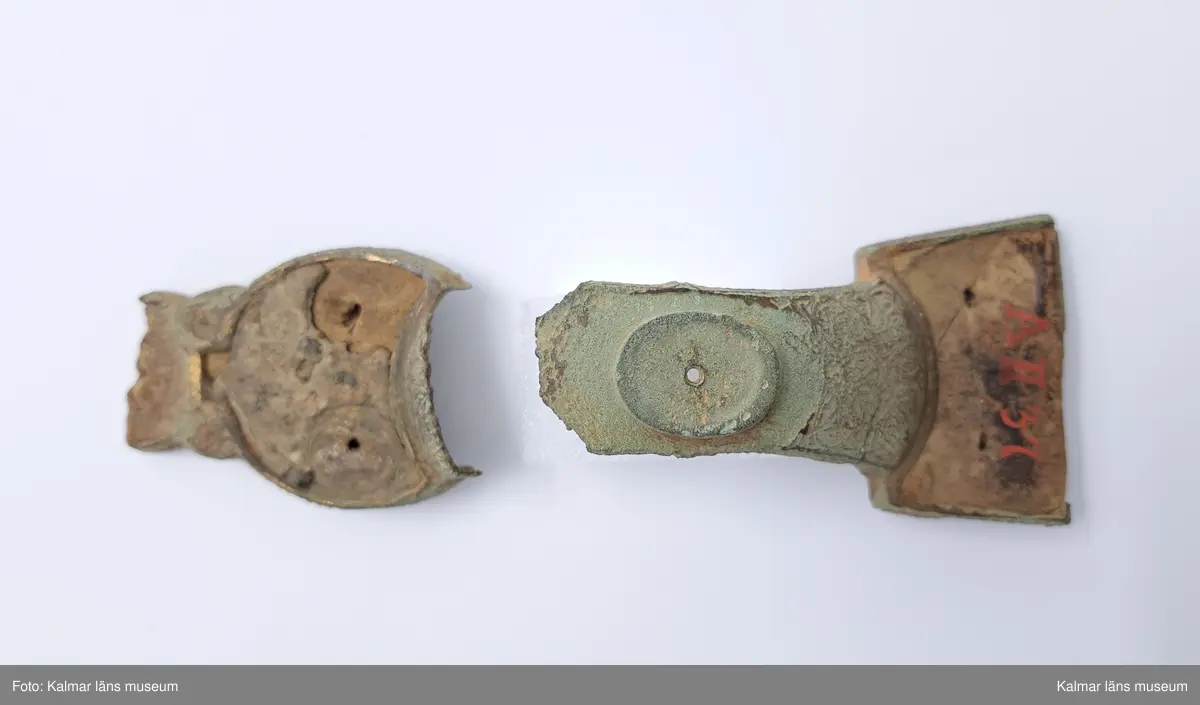 KLM 232. Spänne, ryggknappspänne. Gjutet av brons. Ryggknapp och skiva samt ungefär hälften av nedersta rundeln fattas. Bågen är avbruten. Fyllningen i de fördjupade partierna ligger kvar och täcks delvis av bronsbleck. Spår av förgyllning. På kanterna ornering med rutmönster och på bygeln med slingrande ornament.