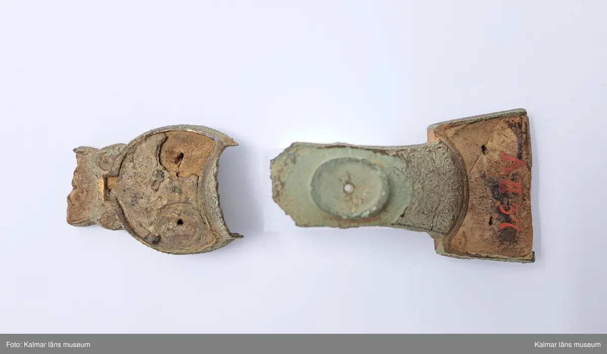 KLM 232. Spänne, ryggknappspänne. Gjutet av brons. Ryggknapp och skiva samt ungefär hälften av nedersta rundeln fattas. Bågen är avbruten. Fyllningen i de fördjupade partierna ligger kvar och täcks delvis av bronsbleck. Spår av förgyllning. På kanterna ornering med rutmönster och på bygeln med slingrande ornament.