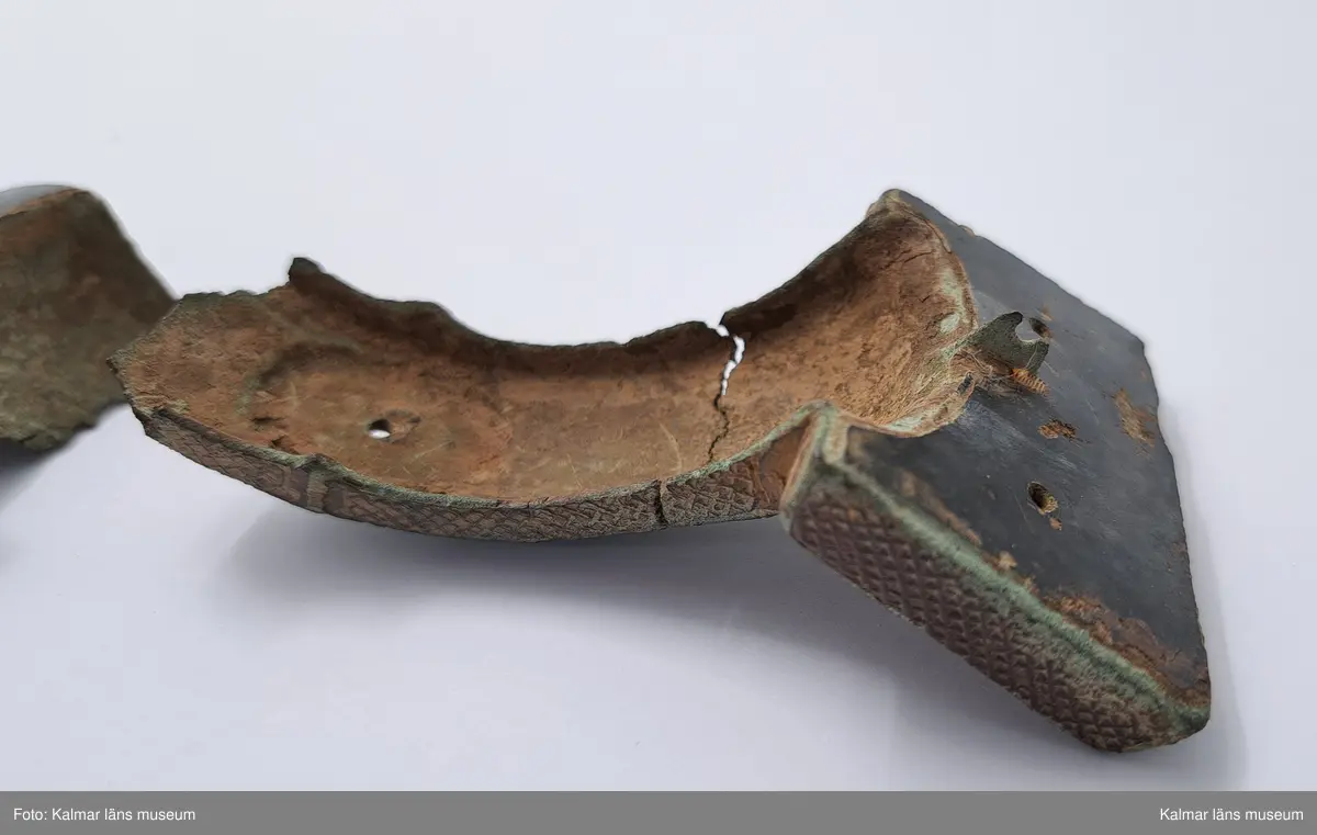 KLM 232. Spänne, ryggknappspänne. Gjutet av brons. Ryggknapp och skiva samt ungefär hälften av nedersta rundeln fattas. Bågen är avbruten. Fyllningen i de fördjupade partierna ligger kvar och täcks delvis av bronsbleck. Spår av förgyllning. På kanterna ornering med rutmönster och på bygeln med slingrande ornament.