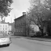 Utmed Kungsgatan i Linköping 1965. Då hade en omfattande sanering av kvarteret Baggens äldre bebyggelse fortgått en längre tid och stora ytor gapade tomma. Inom kort skulle även det lilla gatuhuset till Kungsgatan 26 komma att rivas.