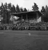 Gymnastikuppvisningen, 25/5 1941. 
Publikbild, med hedersläktaren, på Värendsvallen. Man skymtar en vitklädd
kvinna i mitten som talar.