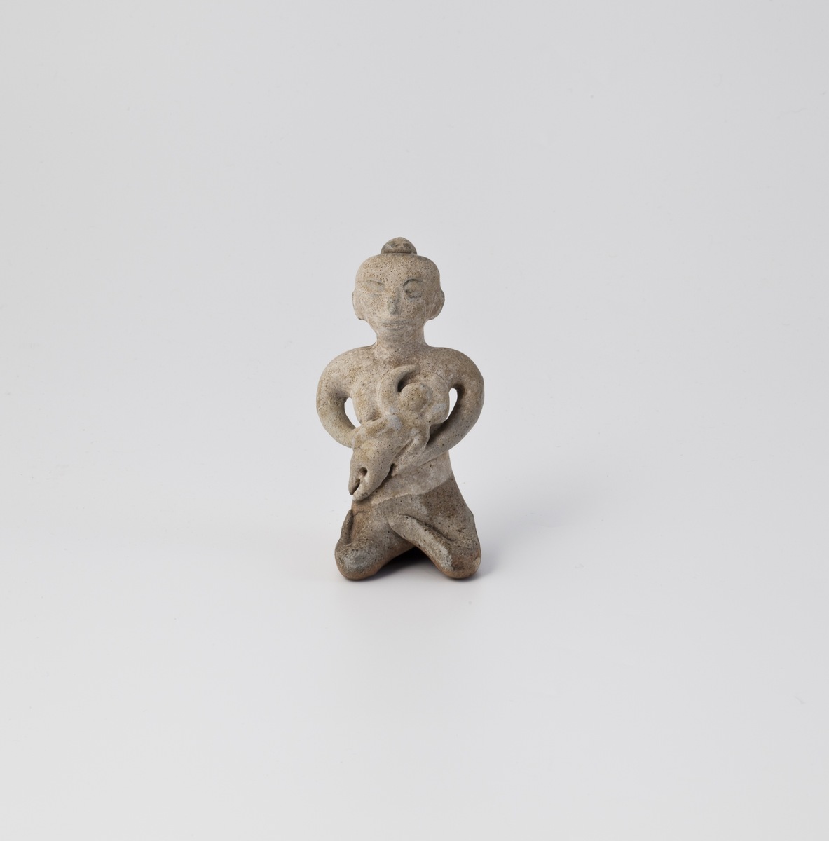 Figur i leirgods som representerer en ammende kvinne med stiliserte trekk. Figuren er hul, og har rester av glasur enkelte steder.
