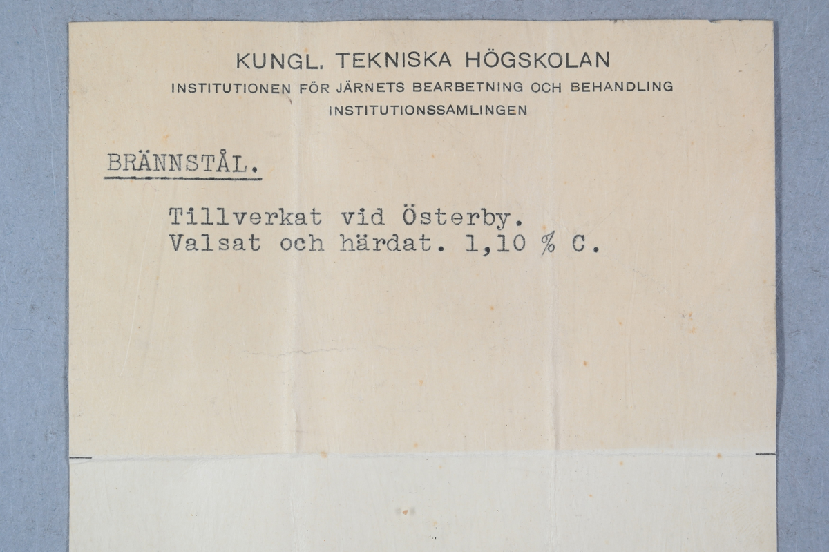 Prov på brännstål. Påklistrad lapp med notering: "Österby, Brännstål, valsadt, härdat, C = 1,10%." Tillhörande lapp med notering: "Brännstål. Tillverkat vid Österby. Valsat och härdat. 1,10 % C."