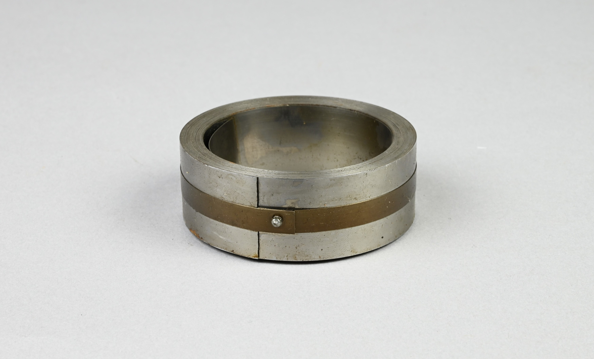 Prov på härdat bandstål. Två tillhörande lappar med notering: "Härdat bandstål för rakknivblad. 22,2 x 0,15 mm. Tillverkat vid Munkfors bruk, Uddeholms AB."