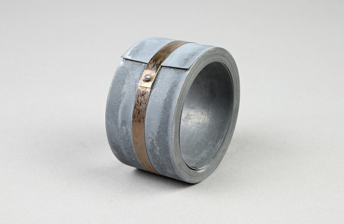 Prov på förblyat bandjärn. Två tillhörande lappar med notering: "Förblyat bandjärn. 34 x 0,32 mm. Martin 0,20 % C. Tillverkat vid Munkfors bruk, Uddeholms AB."