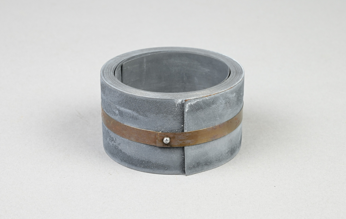 Prov på förblyat bandjärn. Två tillhörande lappar med notering: "Förblyat bandjärn. 34 x 0,32 mm. Martin 0,20 % C. Tillverkat vid Munkfors bruk, Uddeholms AB."