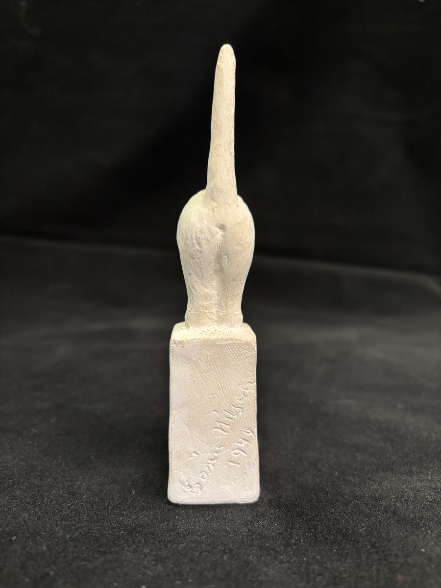 Gipsskulptur som föreställer en katt stående på en hög sockel.
Katten står med lätt böjd rygg och med svansen rakt upp.
På sockelns ena sida finns Carin Nilsons signering samt årtalet 1949.