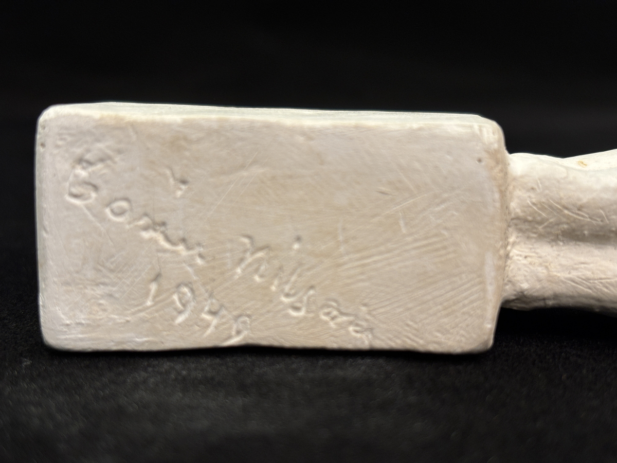 Gipsskulptur som föreställer en katt stående på en hög sockel.
Katten står med lätt böjd rygg och med svansen rakt upp.
På sockelns ena sida finns Carin Nilsons signering samt årtalet 1949.