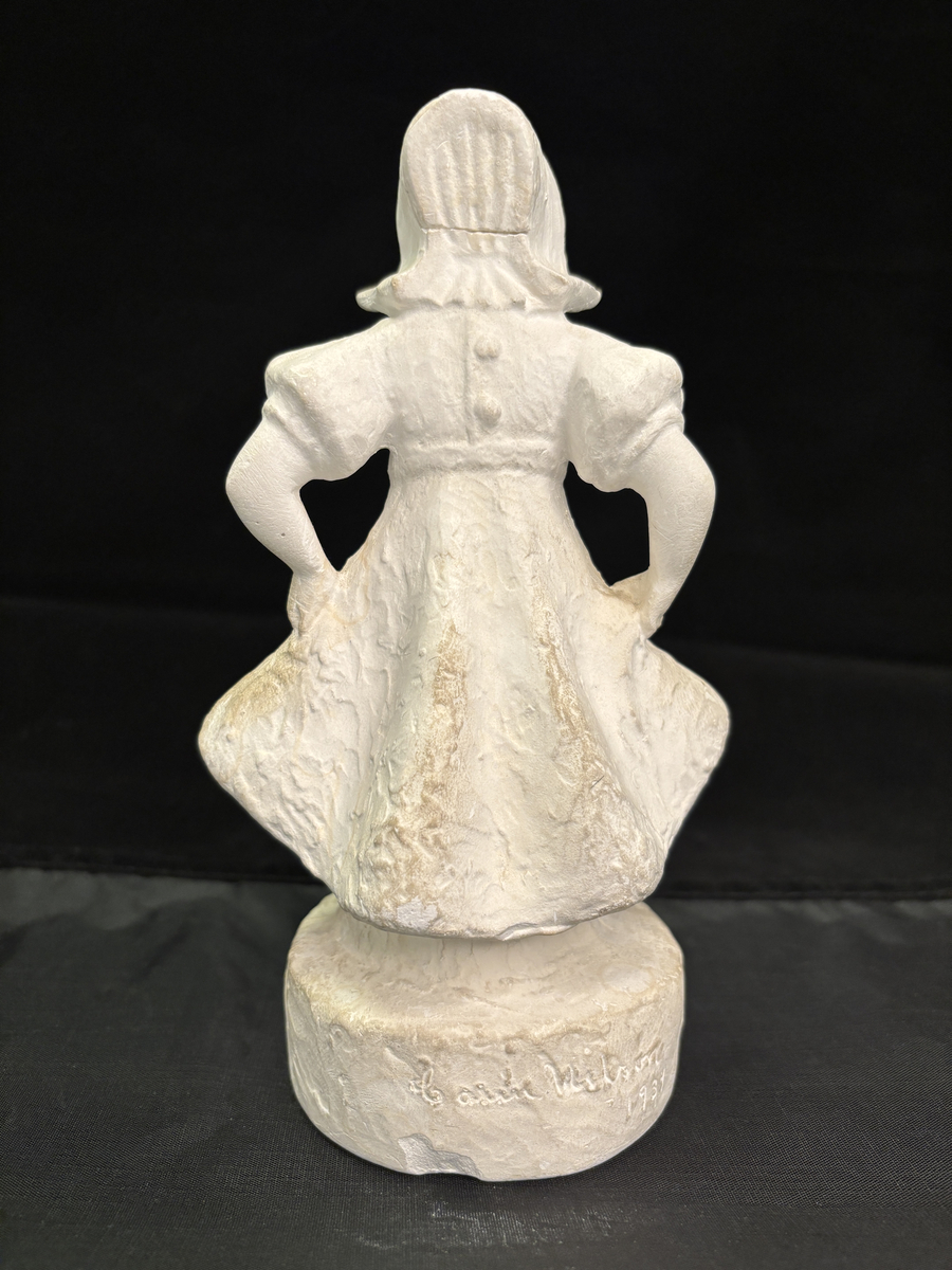 Gipsfigur. Skulptur som föreställer en flicka, stående på en sockel.
Flickan visas i helfigur. Hon är klädd i en klänning som hon håller i och ut med händerna och på huvudet har hon en hatt i bahyttstil, med stora brätten på sidorna.
På sockelns framsida står det "Kyss mej om du kan" och på andra sidan finns konstnärens signering: Carin Nilson samt årtal 1934.