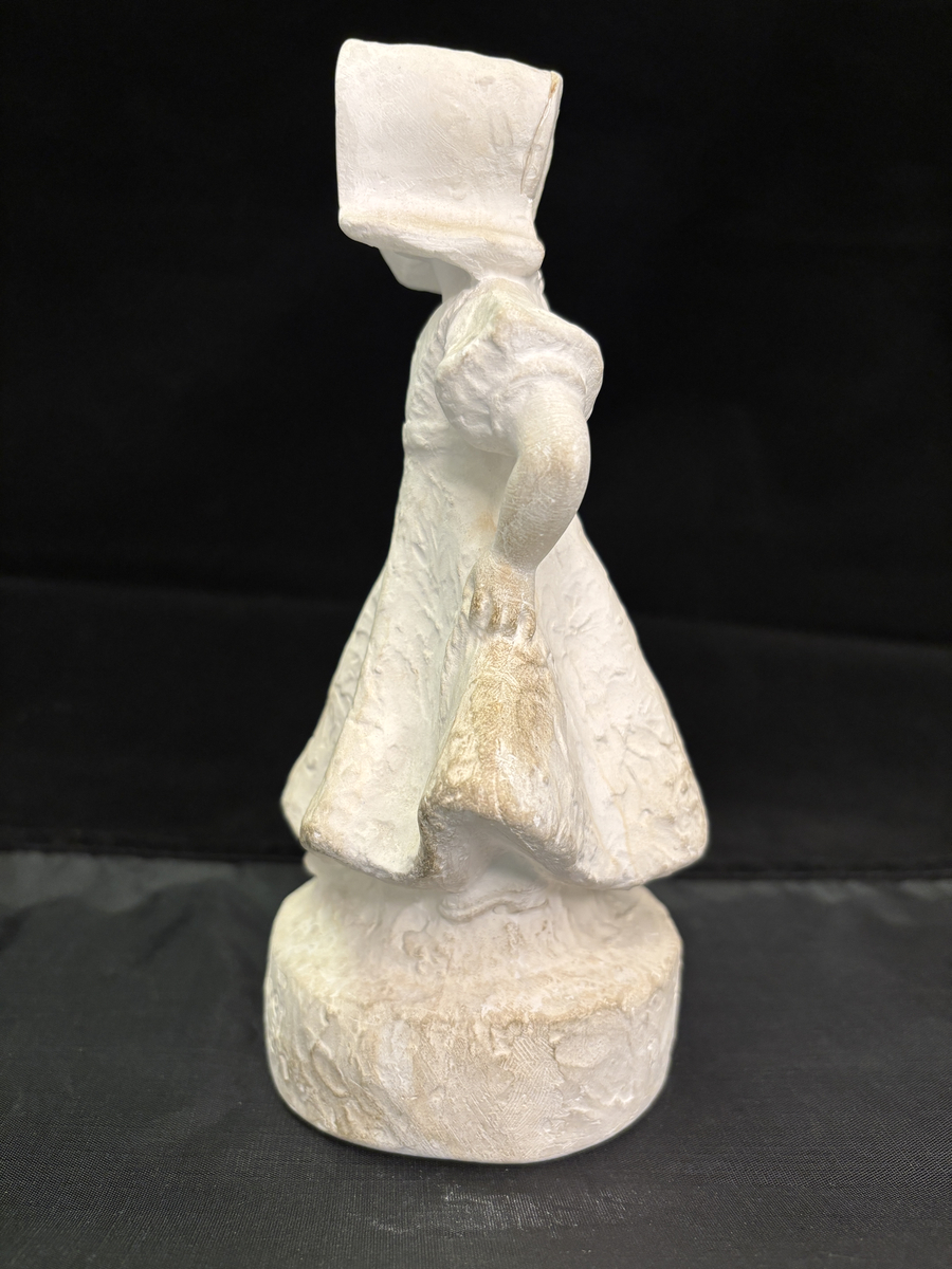 Gipsfigur. Skulptur som föreställer en flicka, stående på en sockel.
Flickan visas i helfigur. Hon är klädd i en klänning som hon håller i och ut med händerna och på huvudet har hon en hatt i bahyttstil, med stora brätten på sidorna.
På sockelns framsida står det "Kyss mej om du kan" och på andra sidan finns konstnärens signering: Carin Nilson samt årtal 1934.