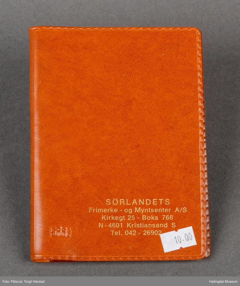 Frimerkealbum, eller -hefte produsert av eller for Sørlandets Frimerke- og Myntsenter A/S, Kristiansand. Dette, og kontaktinfo, er skrevet i gull. Det er også en påklistret, hvit prislapp i høyre hjørne med prisen 10.00 kr. Hefte er laget i rødbrun plast som skal se ut som lær. Innsiden er et ringhefte med plastringer i ryggen. Sidene er laget for frimerker og flere norske frimerker er sortert på noen sider. 