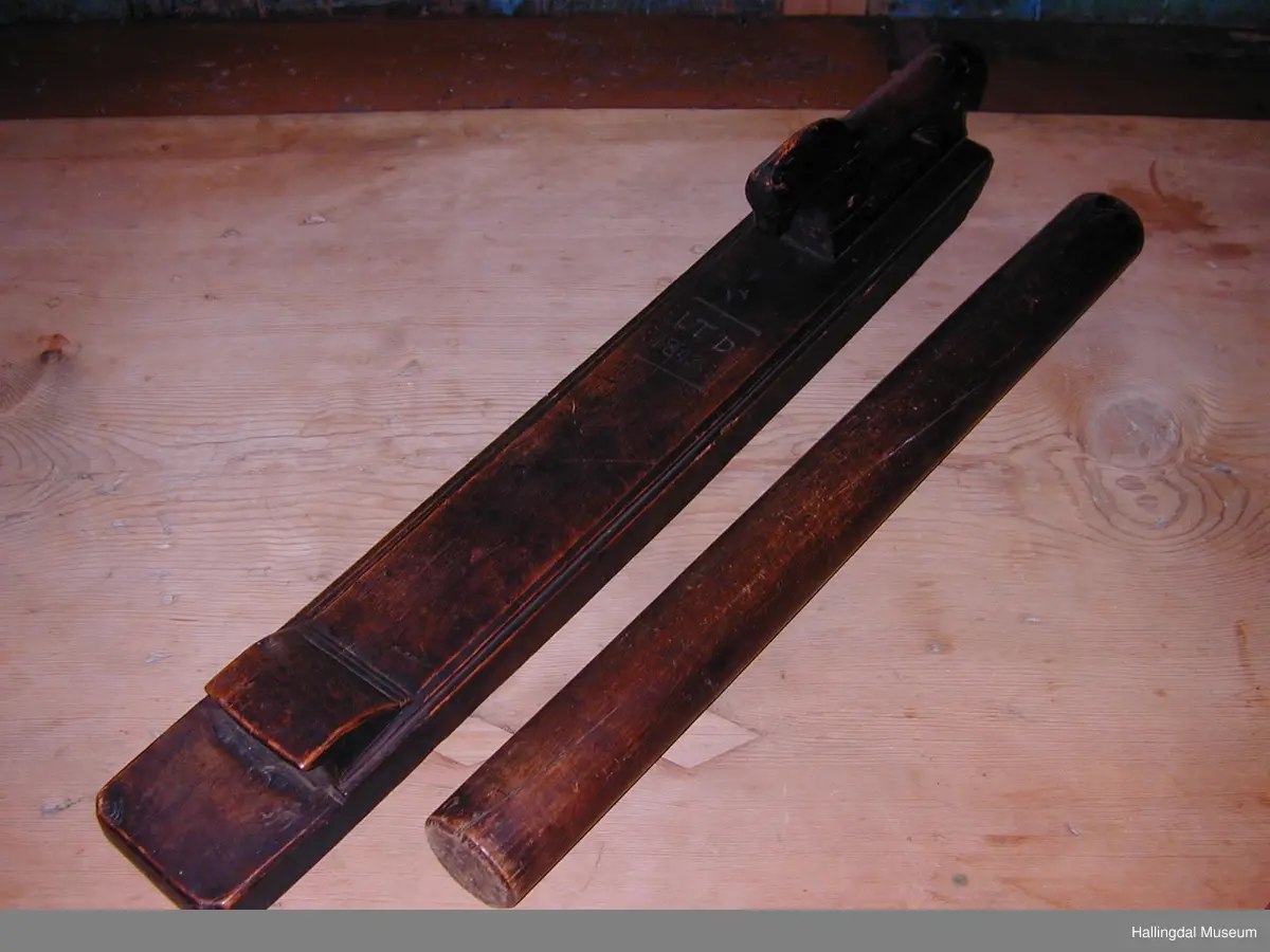 Den eine delen eit rektangulært trestykke, profilerte kantar. På bakre delen ein skoren hest. På framre delen eit handtak. Den andre delen er ein sylindrisk stokk, i eine enden ei lærhempe.