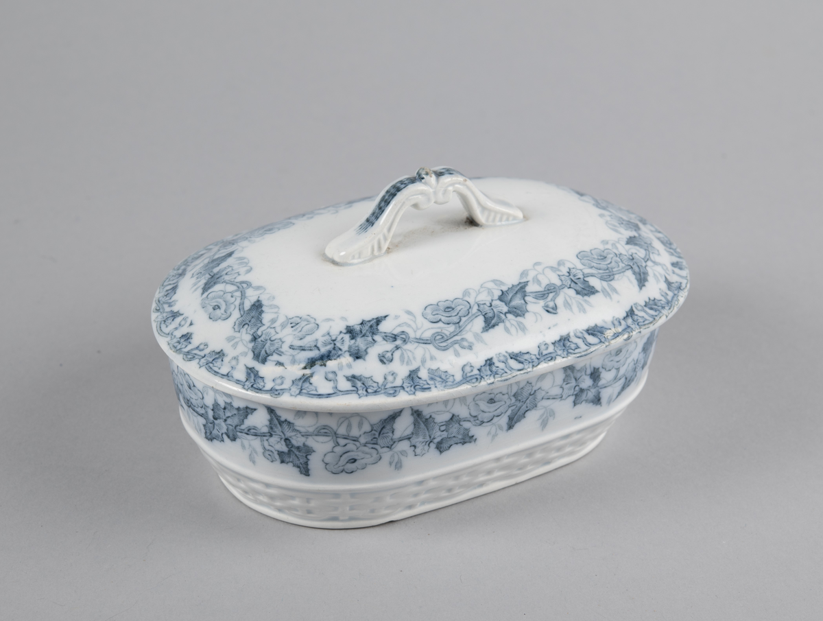 Oval skål med lokk. Inni en skål med gjennomhullet bunn (rist). Trykt dekor utvendig. med motiv av blomster- og bladranker. Nedre del har flettverksmønster i keramikken.