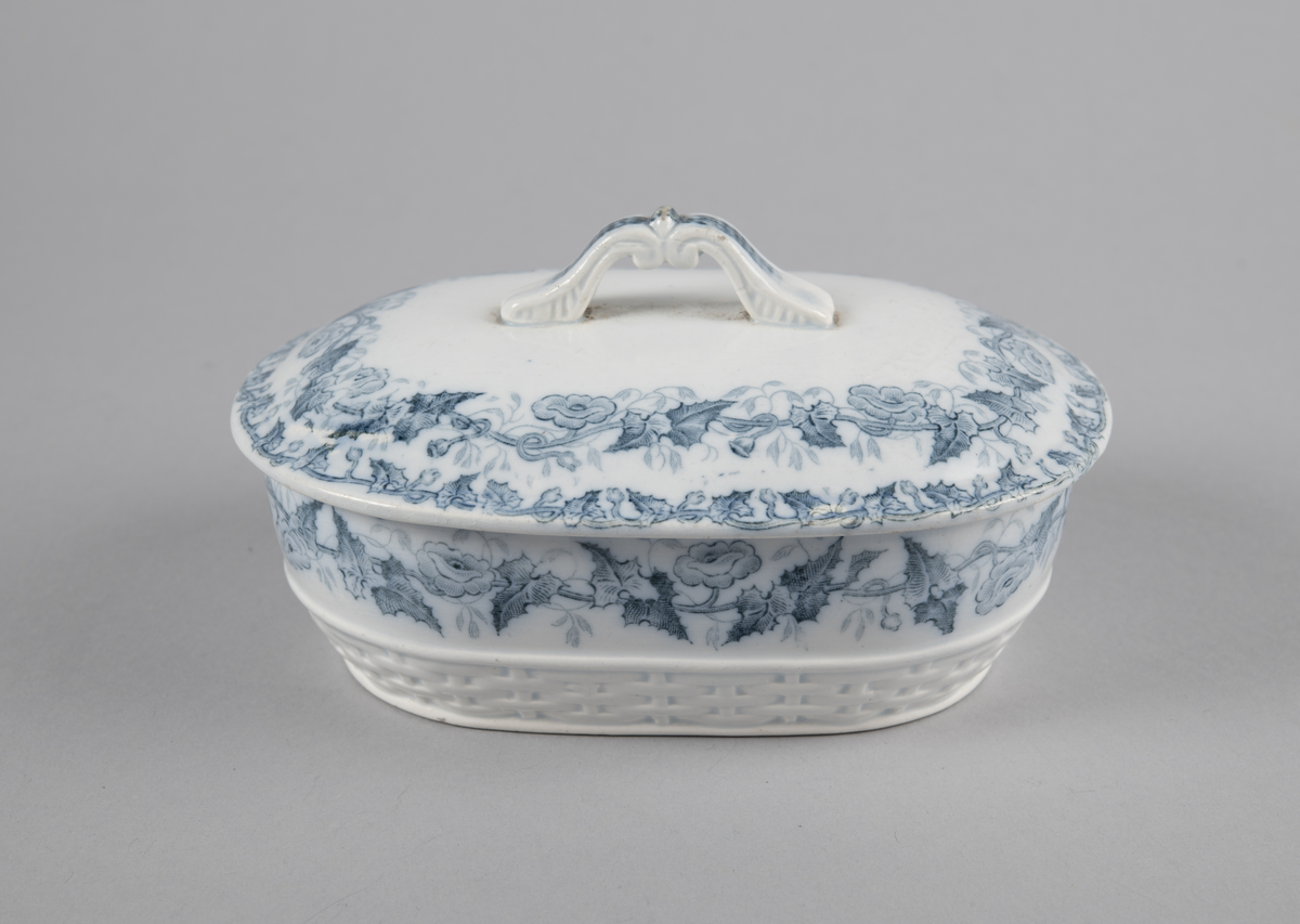 Oval skål med lokk. Inni en skål med gjennomhullet bunn (rist). Trykt dekor utvendig. med motiv av blomster- og bladranker. Nedre del har flettverksmønster i keramikken.