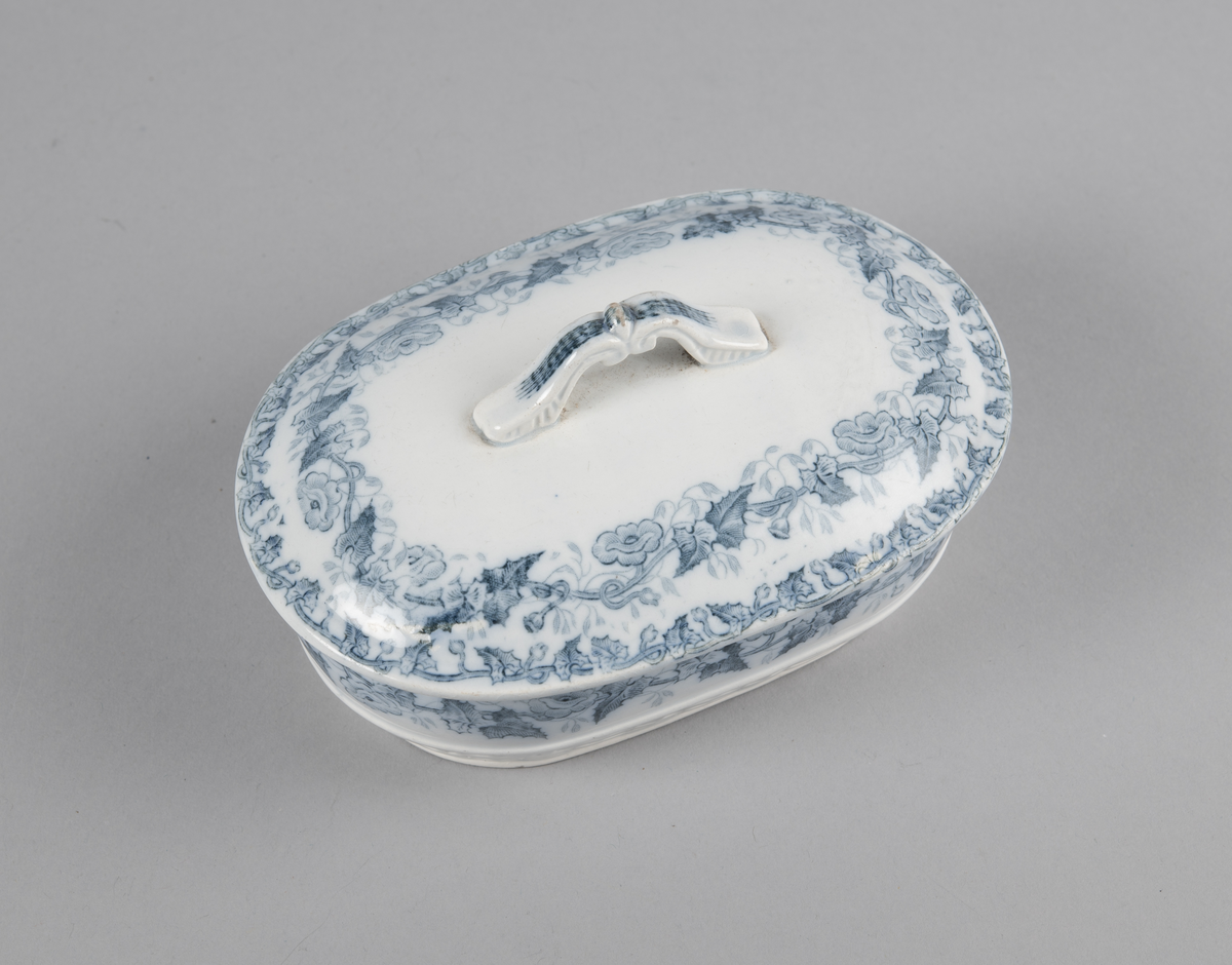Oval skål med lokk. Inni en skål med gjennomhullet bunn (rist). Trykt dekor utvendig. med motiv av blomster- og bladranker. Nedre del har flettverksmønster i keramikken.
