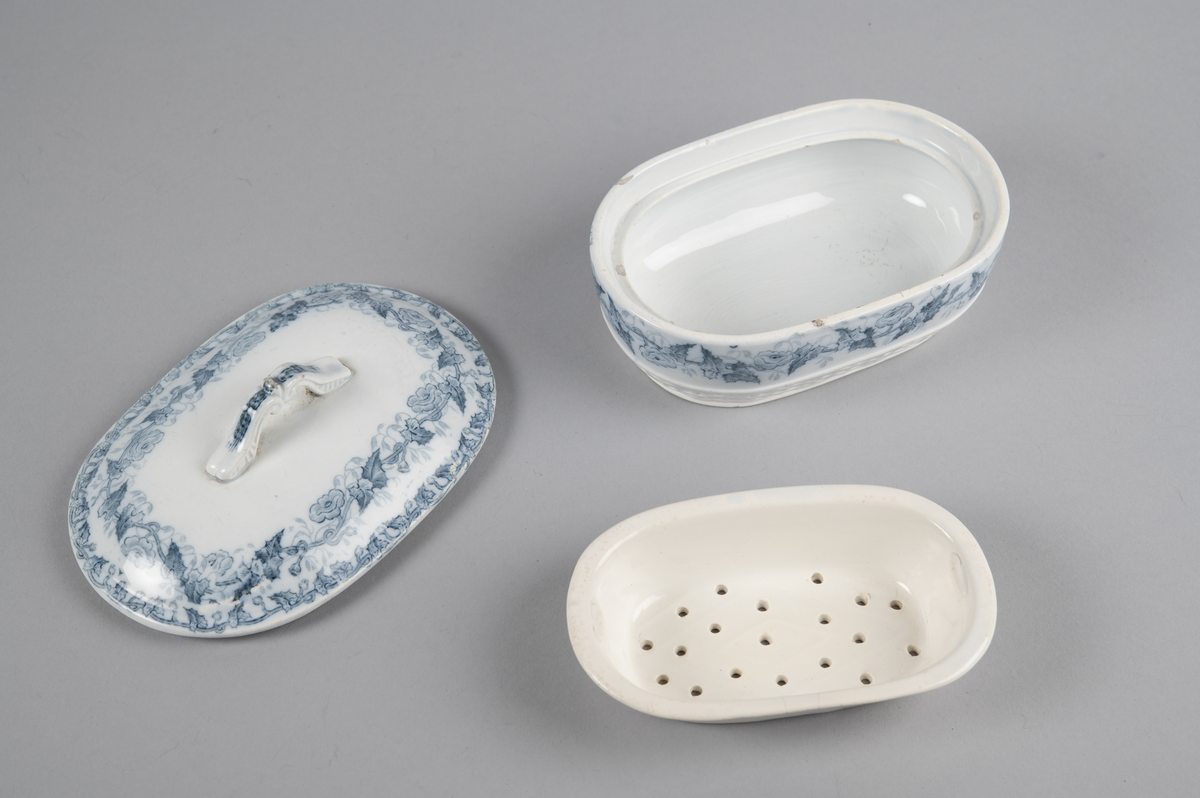 Oval skål med lokk. Inni en skål med gjennomhullet bunn (rist). Trykt dekor utvendig. med motiv av blomster- og bladranker. Nedre del har flettverksmønster i keramikken.