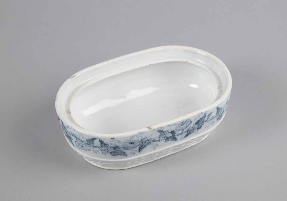 Oval skål med lokk. Inni en skål med gjennomhullet bunn (rist). Trykt dekor utvendig. med motiv av blomster- og bladranker. Nedre del har flettverksmønster i keramikken.