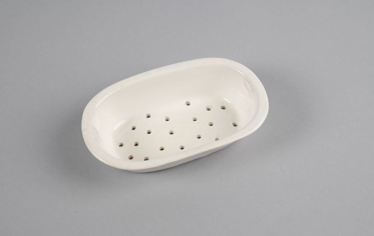 Oval skål med lokk. Inni en skål med gjennomhullet bunn (rist). Trykt dekor utvendig. med motiv av blomster- og bladranker. Nedre del har flettverksmønster i keramikken.