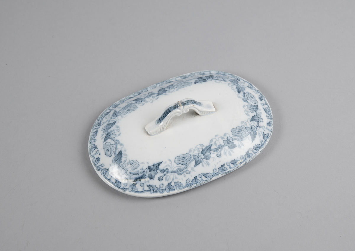 Oval skål med lokk. Inni en skål med gjennomhullet bunn (rist). Trykt dekor utvendig. med motiv av blomster- og bladranker. Nedre del har flettverksmønster i keramikken.