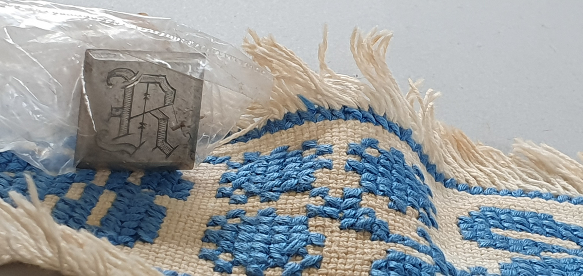 Ostebånd i bomull til 4-kilosost. Brodert i korssting på sultanstoff. Sølvstift følger med.