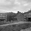 Linköping 1965 och ett av många exempel av rivningsytor i staden vid tiden. I kvarteret Braxen hade byggnadsarbetena av det gigantiskt EPA-varuhuset med vidliggande kontorsytor påbörjats. Byggnadskomplexet skulle komma att fylla närmast hela kvarterets utbredning och därtill krävdes omfattande rivningar av den föregående bebyggelsen. Här en vy längs kvarterets sträckning utmed Snickaregatan, där de gamla trähusen Snickaregatan 18 och 20 stod i tur att rivas.