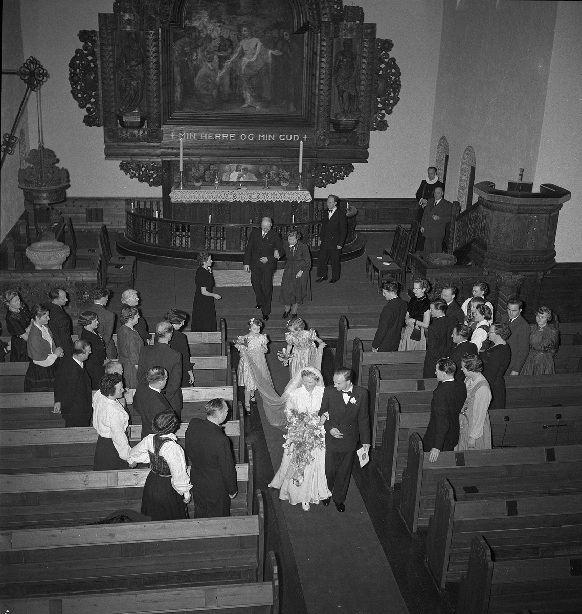 Bryllup i Rjukan kirke mellom Hans Mæland og Borghild Roland. Brudeparet er på vei ut midtgangen, brudepiker holder brudens slør. Bryllupsfølge stående på hver side av midtgangen.