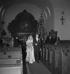 Bryllup i Rjukan kirke for ekteparet Jansen. Brudeparet gående ut midtgangen med altertavlen i bakgrunnen. Bryllupsgjestene står oppreist langs benkeradene.