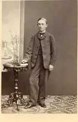 Porträtt av en ung man som står vid ett bord.