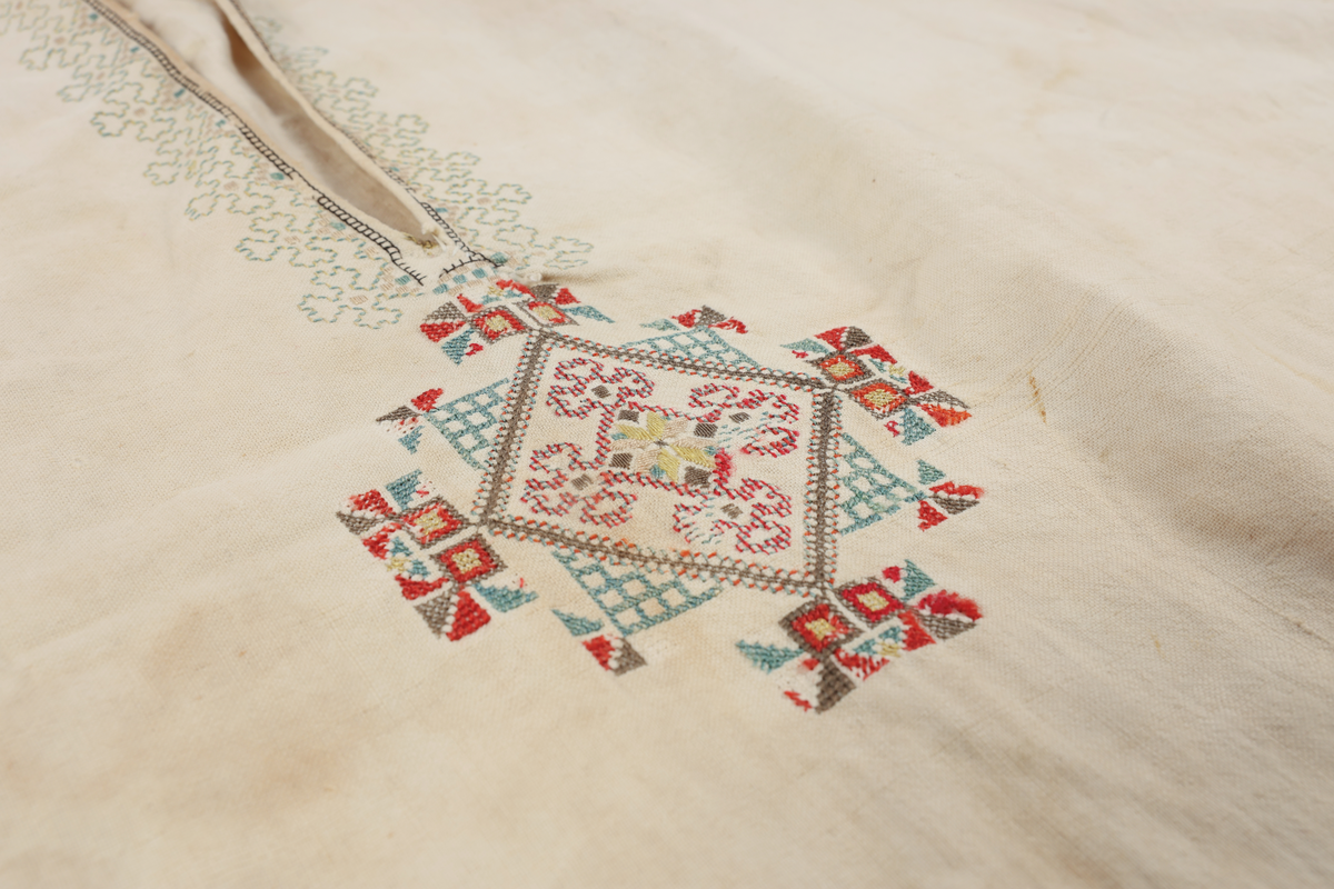Hvit mannsskjorte med flerfarget broderi som dekor på krave og lengs halssplitt.