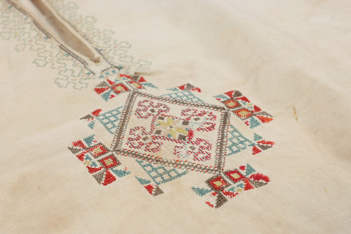 Hvit mannsskjorte med flerfarget broderi som dekor på krave og lengs halssplitt.