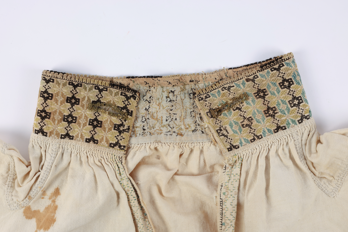 Hvit mannsskjorte med flerfarget broderi som dekor på krave og lengs halssplitt.