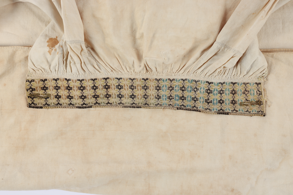 Hvit mannsskjorte med flerfarget broderi som dekor på krave og lengs halssplitt.