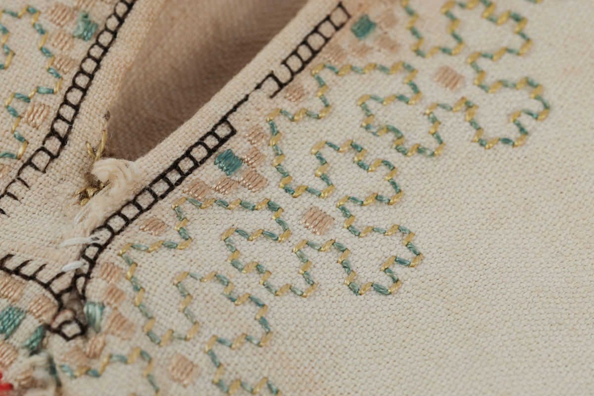 Hvit mannsskjorte med flerfarget broderi som dekor på krave og lengs halssplitt.