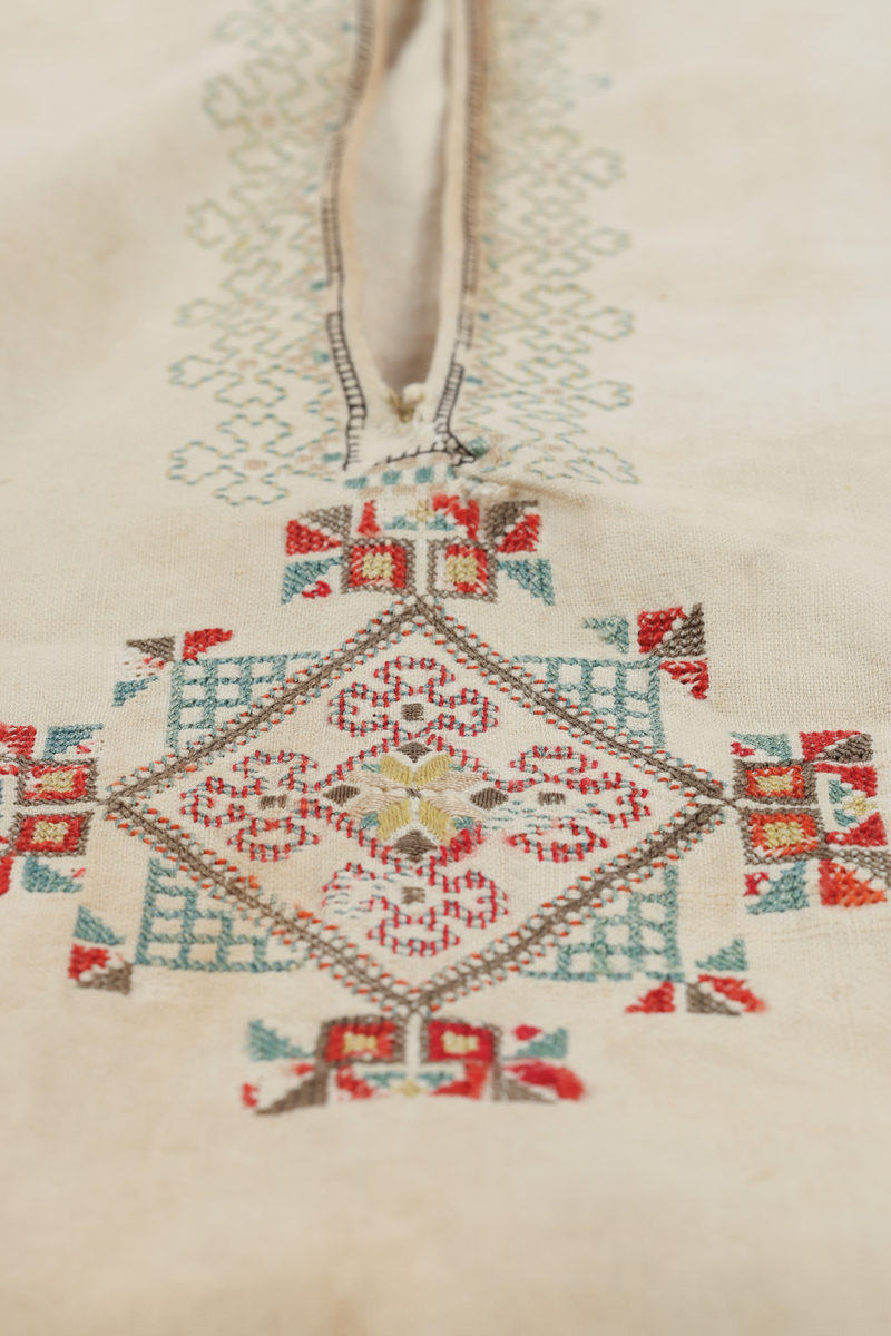Hvit mannsskjorte med flerfarget broderi som dekor på krave og lengs halssplitt.