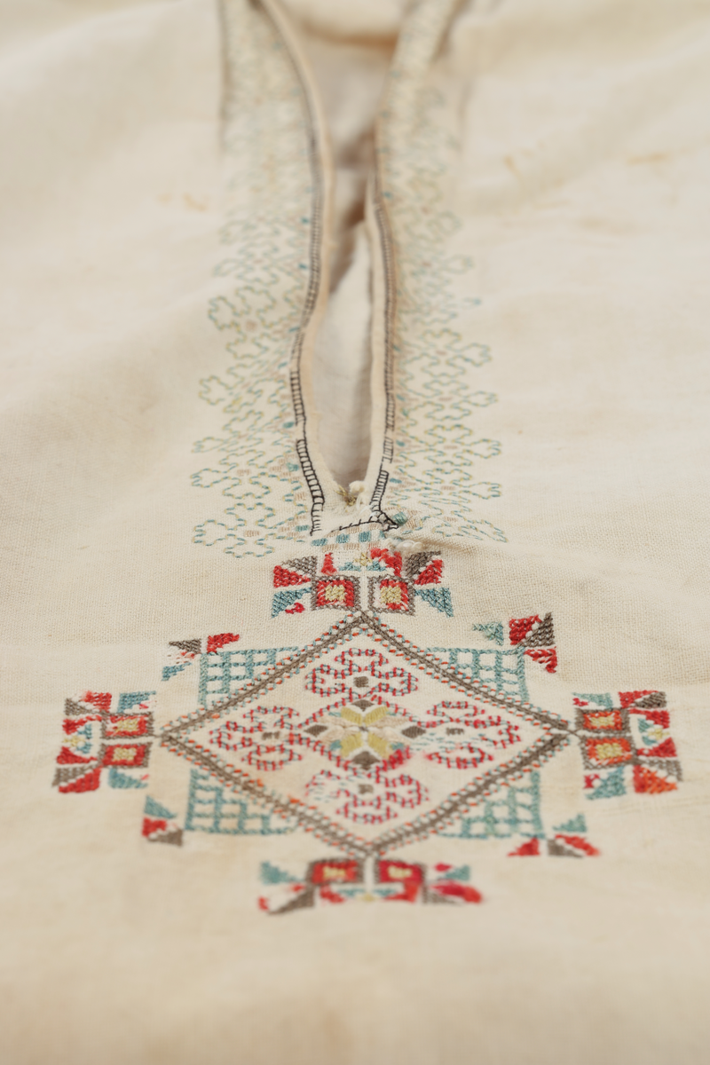 Hvit mannsskjorte med flerfarget broderi som dekor på krave og lengs halssplitt.