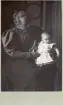 Porträtt av Sally Maria, troligen Rettig i knät på en kvinna, född den 12 okt. 1894 ?? 8 månader gammal (enligt text baksida kort).