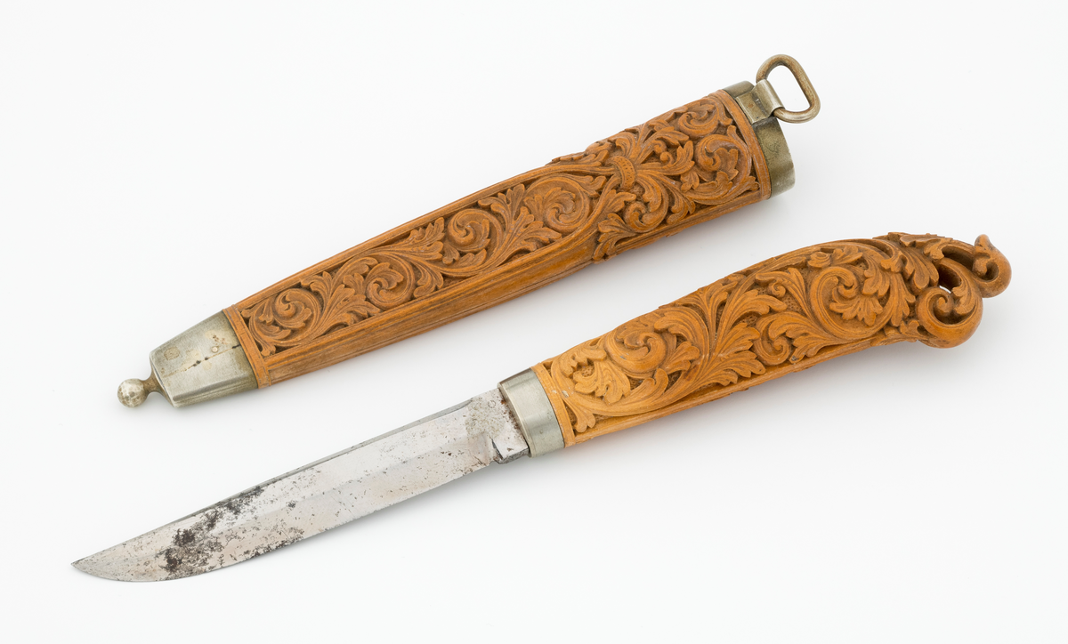 Tollekniv i slire laget av den kjente treskjæreren Ole Olsen Moene (1839-1908) fra Oppdal i Sør-Trøndelag. Kniven har blad som antas å være av jern og stål, mens skaftet og slira er utført i tre, men med beslag av nysølv. 

Kniven er 19,3 centimeter lang. Bladet utgjør 8,9 centimeter av dette lengdemålet. Det er 14,9 millimeter bredt bakerst ved brystningen. Her er tjukkelsen 3,3 millimeter. Bladryggen er noenlunde rettlinjet, men særlig den bakre delen er avfaset mot sidene. Slipefasene er opptil 9 millimeter brede. Bladet er blankpolert. Det har ingen stempler eller andre signaturer som tydeliggjør produsenten, men mye tyder vel på at dette er et «fabrikkblad» - altså en masseprodusert komponent.

Tangen i den bakre enden av skaftet er tappet inn i et snaut 10,5 centimeter langt skaft, lagd av det for nordmenn eksotiske treslaget buksbom (Buxus sempervirens). Dette er en buskvekst som har sin opprinnelige utbredelse i det submeriterrane området. Den fremre skaftenden er forsterket med en 7 millimeter bred skaftholk med glatt overflate. Skaftet er konvekst i formen, og det har, som på knivskaft flest, et ovalt tverrsnitt. Den bakre skaftenden er en aning krum - mot buksida. Skaftet har flatedekkende utskåret dekor, elegant formete akantusranker i cirka 2 millimeter høyt relieff, organisert på to flater, ei på hver av skaftets «bredsider». I den bakre enden er akantusbladene gjennombrudte. 

Slira er et 14,4 centimeter langt hylster, sammensatt av to buete buksbomplater med buete tverrsnitt, holdt ihop av en 5,7 millimeter bred munningsholk i den øvre enden og en 2,6 centimeter høy doppsko med endeknopp i den nedre enden. Bøde doppskoen og munningsholken har glatte overflater. De to buksbomskiene har flatedekkende akantusdekor. På de delene som skal omslutte bladet er akantusrankene innrammet av to ribber som møtes cirka 3,5 centimeter under sliremunningen. Fra disse punktene voksder det rosetter som omgir den nedre (fremre) enden av knivskaftet. På slira er akantusrelieffene om lag 1 millimeter høye. På baksida av munningsholken er detr påloddet ei hempe for et oppheng, som antakelig har vært av lær. Dette opphenget mangler.

Verken kniven eller slira har signaturer som refererer til produsenten.