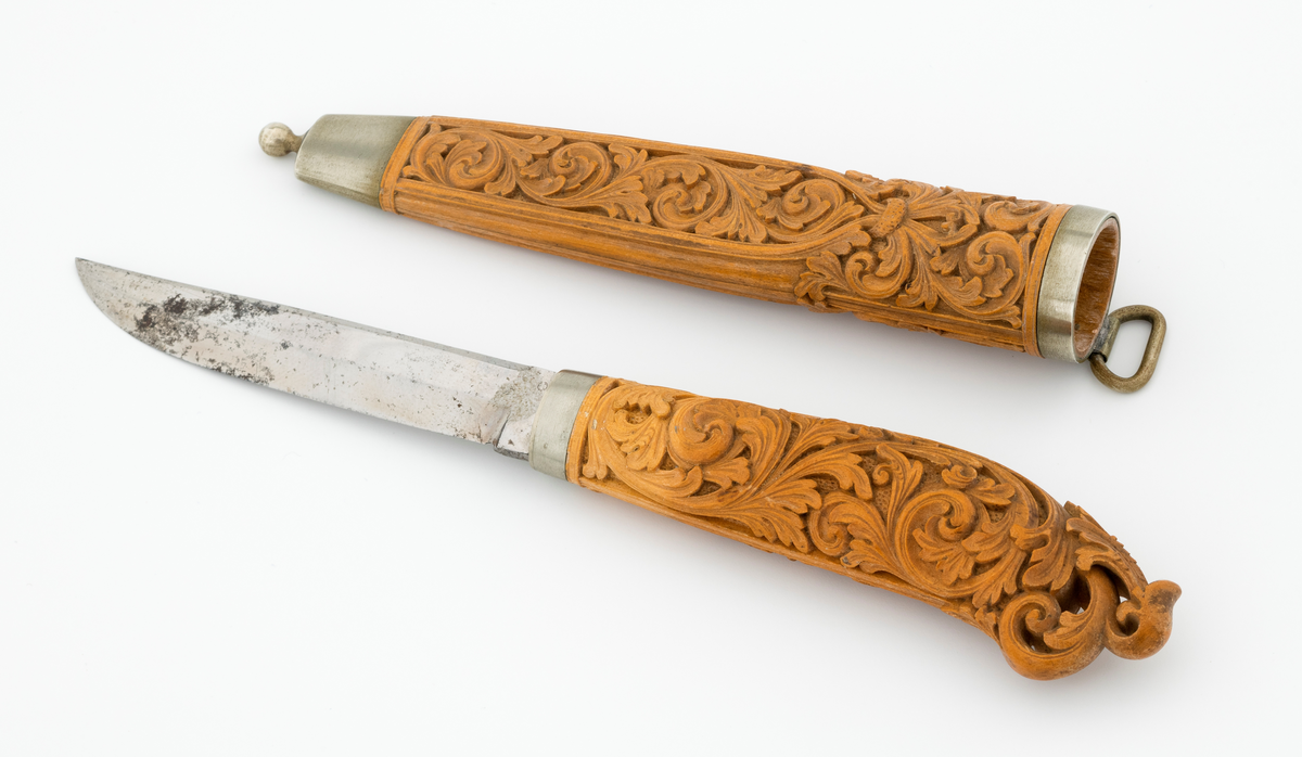 Tollekniv i slire laget av den kjente treskjæreren Ole Olsen Moene (1839-1908) fra Oppdal i Sør-Trøndelag. Kniven har blad som antas å være av jern og stål, mens skaftet og slira er utført i tre, men med beslag av nysølv. 

Kniven er 19,3 centimeter lang. Bladet utgjør 8,9 centimeter av dette lengdemålet. Det er 14,9 millimeter bredt bakerst ved brystningen. Her er tjukkelsen 3,3 millimeter. Bladryggen er noenlunde rettlinjet, men særlig den bakre delen er avfaset mot sidene. Slipefasene er opptil 9 millimeter brede. Bladet er blankpolert. Det har ingen stempler eller andre signaturer som tydeliggjør produsenten, men mye tyder vel på at dette er et «fabrikkblad» - altså en masseprodusert komponent.

Tangen i den bakre enden av skaftet er tappet inn i et snaut 10,5 centimeter langt skaft, lagd av det for nordmenn eksotiske treslaget buksbom (Buxus sempervirens). Dette er en buskvekst som har sin opprinnelige utbredelse i det submeriterrane området. Den fremre skaftenden er forsterket med en 7 millimeter bred skaftholk med glatt overflate. Skaftet er konvekst i formen, og det har, som på knivskaft flest, et ovalt tverrsnitt. Den bakre skaftenden er en aning krum - mot buksida. Skaftet har flatedekkende utskåret dekor, elegant formete akantusranker i cirka 2 millimeter høyt relieff, organisert på to flater, ei på hver av skaftets «bredsider». I den bakre enden er akantusbladene gjennombrudte. 

Slira er et 14,4 centimeter langt hylster, sammensatt av to buete buksbomplater med buete tverrsnitt, holdt ihop av en 5,7 millimeter bred munningsholk i den øvre enden og en 2,6 centimeter høy doppsko med endeknopp i den nedre enden. Bøde doppskoen og munningsholken har glatte overflater. De to buksbomskiene har flatedekkende akantusdekor. På de delene som skal omslutte bladet er akantusrankene innrammet av to ribber som møtes cirka 3,5 centimeter under sliremunningen. Fra disse punktene voksder det rosetter som omgir den nedre (fremre) enden av knivskaftet. På slira er akantusrelieffene om lag 1 millimeter høye. På baksida av munningsholken er detr påloddet ei hempe for et oppheng, som antakelig har vært av lær. Dette opphenget mangler.

Verken kniven eller slira har signaturer som refererer til produsenten.