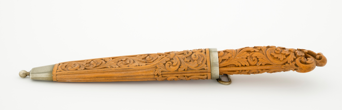 Tollekniv i slire laget av den kjente treskjæreren Ole Olsen Moene (1839-1908) fra Oppdal i Sør-Trøndelag. Kniven har blad som antas å være av jern og stål, mens skaftet og slira er utført i tre, men med beslag av nysølv. 

Kniven er 19,3 centimeter lang. Bladet utgjør 8,9 centimeter av dette lengdemålet. Det er 14,9 millimeter bredt bakerst ved brystningen. Her er tjukkelsen 3,3 millimeter. Bladryggen er noenlunde rettlinjet, men særlig den bakre delen er avfaset mot sidene. Slipefasene er opptil 9 millimeter brede. Bladet er blankpolert. Det har ingen stempler eller andre signaturer som tydeliggjør produsenten, men mye tyder vel på at dette er et «fabrikkblad» - altså en masseprodusert komponent.

Tangen i den bakre enden av skaftet er tappet inn i et snaut 10,5 centimeter langt skaft, lagd av det for nordmenn eksotiske treslaget buksbom (Buxus sempervirens). Dette er en buskvekst som har sin opprinnelige utbredelse i det submeriterrane området. Den fremre skaftenden er forsterket med en 7 millimeter bred skaftholk med glatt overflate. Skaftet er konvekst i formen, og det har, som på knivskaft flest, et ovalt tverrsnitt. Den bakre skaftenden er en aning krum - mot buksida. Skaftet har flatedekkende utskåret dekor, elegant formete akantusranker i cirka 2 millimeter høyt relieff, organisert på to flater, ei på hver av skaftets «bredsider». I den bakre enden er akantusbladene gjennombrudte. 

Slira er et 14,4 centimeter langt hylster, sammensatt av to buete buksbomplater med buete tverrsnitt, holdt ihop av en 5,7 millimeter bred munningsholk i den øvre enden og en 2,6 centimeter høy doppsko med endeknopp i den nedre enden. Bøde doppskoen og munningsholken har glatte overflater. De to buksbomskiene har flatedekkende akantusdekor. På de delene som skal omslutte bladet er akantusrankene innrammet av to ribber som møtes cirka 3,5 centimeter under sliremunningen. Fra disse punktene voksder det rosetter som omgir den nedre (fremre) enden av knivskaftet. På slira er akantusrelieffene om lag 1 millimeter høye. På baksida av munningsholken er detr påloddet ei hempe for et oppheng, som antakelig har vært av lær. Dette opphenget mangler.

Verken kniven eller slira har signaturer som refererer til produsenten.