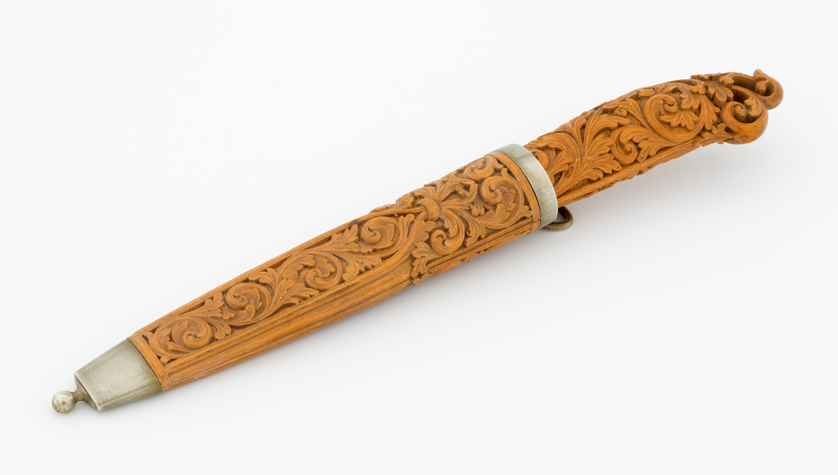 Tollekniv i slire laget av den kjente treskjæreren Ole Olsen Moene (1839-1908) fra Oppdal i Sør-Trøndelag. Kniven har blad som antas å være av jern og stål, mens skaftet og slira er utført i tre, men med beslag av nysølv. 

Kniven er 19,3 centimeter lang. Bladet utgjør 8,9 centimeter av dette lengdemålet. Det er 14,9 millimeter bredt bakerst ved brystningen. Her er tjukkelsen 3,3 millimeter. Bladryggen er noenlunde rettlinjet, men særlig den bakre delen er avfaset mot sidene. Slipefasene er opptil 9 millimeter brede. Bladet er blankpolert. Det har ingen stempler eller andre signaturer som tydeliggjør produsenten, men mye tyder vel på at dette er et «fabrikkblad» - altså en masseprodusert komponent.

Tangen i den bakre enden av skaftet er tappet inn i et snaut 10,5 centimeter langt skaft, lagd av det for nordmenn eksotiske treslaget buksbom (Buxus sempervirens). Dette er en buskvekst som har sin opprinnelige utbredelse i det submeriterrane området. Den fremre skaftenden er forsterket med en 7 millimeter bred skaftholk med glatt overflate. Skaftet er konvekst i formen, og det har, som på knivskaft flest, et ovalt tverrsnitt. Den bakre skaftenden er en aning krum - mot buksida. Skaftet har flatedekkende utskåret dekor, elegant formete akantusranker i cirka 2 millimeter høyt relieff, organisert på to flater, ei på hver av skaftets «bredsider». I den bakre enden er akantusbladene gjennombrudte. 

Slira er et 14,4 centimeter langt hylster, sammensatt av to buete buksbomplater med buete tverrsnitt, holdt ihop av en 5,7 millimeter bred munningsholk i den øvre enden og en 2,6 centimeter høy doppsko med endeknopp i den nedre enden. Bøde doppskoen og munningsholken har glatte overflater. De to buksbomskiene har flatedekkende akantusdekor. På de delene som skal omslutte bladet er akantusrankene innrammet av to ribber som møtes cirka 3,5 centimeter under sliremunningen. Fra disse punktene voksder det rosetter som omgir den nedre (fremre) enden av knivskaftet. På slira er akantusrelieffene om lag 1 millimeter høye. På baksida av munningsholken er detr påloddet ei hempe for et oppheng, som antakelig har vært av lær. Dette opphenget mangler.

Verken kniven eller slira har signaturer som refererer til produsenten.
