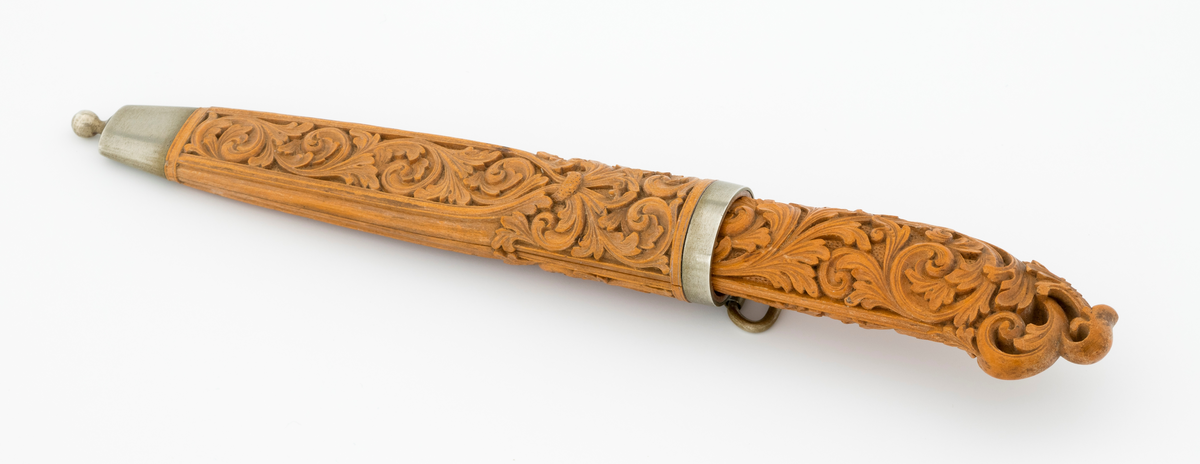 Tollekniv i slire laget av den kjente treskjæreren Ole Olsen Moene (1839-1908) fra Oppdal i Sør-Trøndelag. Kniven har blad som antas å være av jern og stål, mens skaftet og slira er utført i tre, men med beslag av nysølv. 

Kniven er 19,3 centimeter lang. Bladet utgjør 8,9 centimeter av dette lengdemålet. Det er 14,9 millimeter bredt bakerst ved brystningen. Her er tjukkelsen 3,3 millimeter. Bladryggen er noenlunde rettlinjet, men særlig den bakre delen er avfaset mot sidene. Slipefasene er opptil 9 millimeter brede. Bladet er blankpolert. Det har ingen stempler eller andre signaturer som tydeliggjør produsenten, men mye tyder vel på at dette er et «fabrikkblad» - altså en masseprodusert komponent.

Tangen i den bakre enden av skaftet er tappet inn i et snaut 10,5 centimeter langt skaft, lagd av det for nordmenn eksotiske treslaget buksbom (Buxus sempervirens). Dette er en buskvekst som har sin opprinnelige utbredelse i det submeriterrane området. Den fremre skaftenden er forsterket med en 7 millimeter bred skaftholk med glatt overflate. Skaftet er konvekst i formen, og det har, som på knivskaft flest, et ovalt tverrsnitt. Den bakre skaftenden er en aning krum - mot buksida. Skaftet har flatedekkende utskåret dekor, elegant formete akantusranker i cirka 2 millimeter høyt relieff, organisert på to flater, ei på hver av skaftets «bredsider». I den bakre enden er akantusbladene gjennombrudte. 

Slira er et 14,4 centimeter langt hylster, sammensatt av to buete buksbomplater med buete tverrsnitt, holdt ihop av en 5,7 millimeter bred munningsholk i den øvre enden og en 2,6 centimeter høy doppsko med endeknopp i den nedre enden. Bøde doppskoen og munningsholken har glatte overflater. De to buksbomskiene har flatedekkende akantusdekor. På de delene som skal omslutte bladet er akantusrankene innrammet av to ribber som møtes cirka 3,5 centimeter under sliremunningen. Fra disse punktene voksder det rosetter som omgir den nedre (fremre) enden av knivskaftet. På slira er akantusrelieffene om lag 1 millimeter høye. På baksida av munningsholken er detr påloddet ei hempe for et oppheng, som antakelig har vært av lær. Dette opphenget mangler.

Verken kniven eller slira har signaturer som refererer til produsenten.