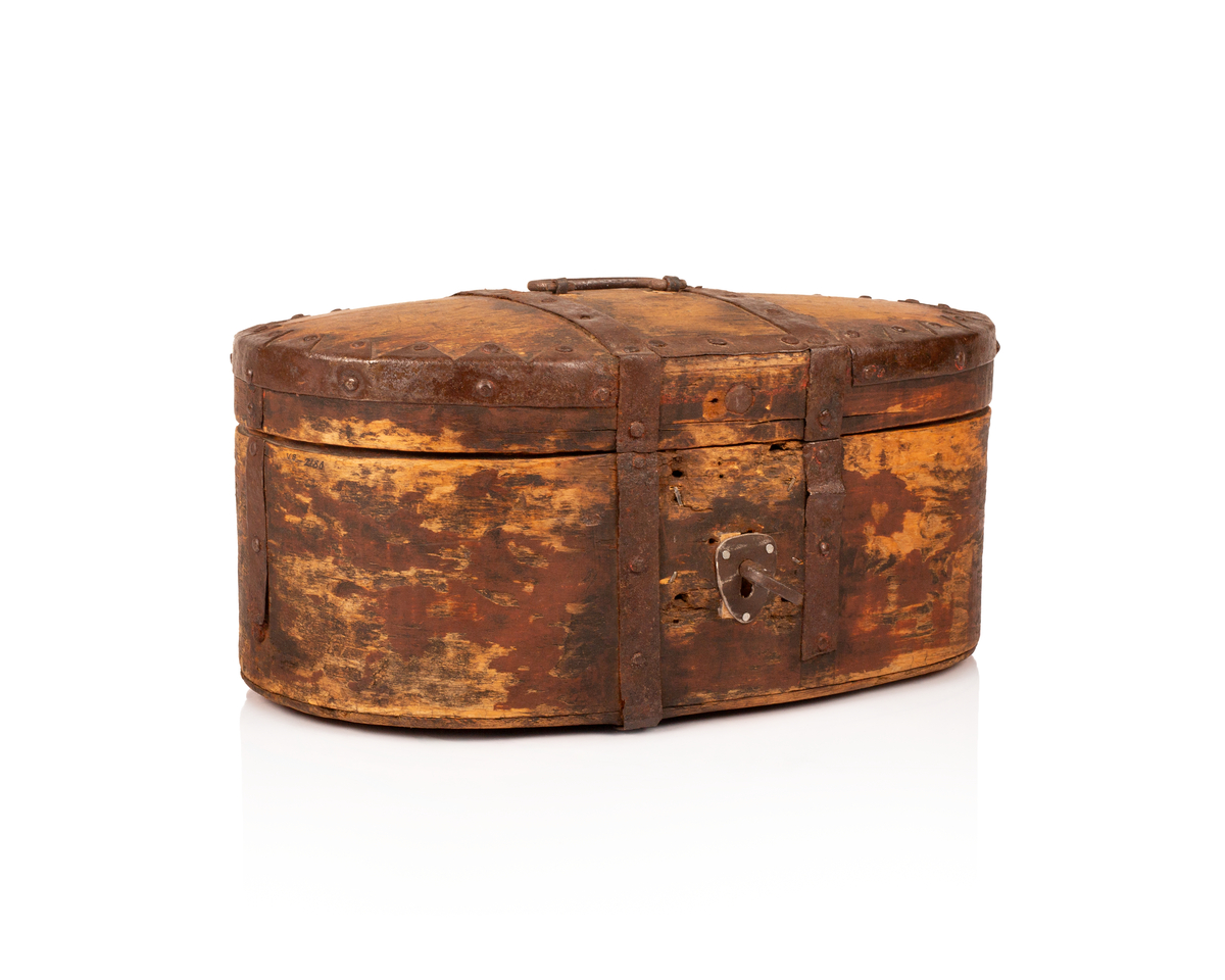 Brun bomme med lås og nøkkel. Den er ovalformet med et svakt hvelvet lokk som er festet med hengsler. Bunnen av bommen er plan. Videre er både bunnen av bommen og toppen av lokket laget av gran, mens sidene er laget av bjørk. 

Lokket og bommens sider er sveipet og består av tynne bjørkelapper, i relativ kraftige dimensjoner, som er brettet sammen for å danne bommens form. Bjørkelappen overlapper hverandre med en god del cm på baksiden og er festet med dobbel nagling. Det er fire nagler i hver av de to rekkene som fester siden sammen. De to rekkene står parallelle overfor hverandre med ca. 5 cm mellomrom. Siden til lokket er festet med en nagle i hver rekke, og i tillegg er det satt inn en nagle nederst på bommen mellom de to rekkene samt en i lokket. 

To smidde jernbånd går fra fremsiden av bommen over lokket og ned på baksiden. På baksiden er det satt inn løkkehengsler i jernbåndene til lokket. Båndene er satt på plass med jernnagler. Rundt toppen av lokket er det et jernbånd som fester lokkets topp og side sammen. Båndet er bøyd over siden, festet med nagler og dekorerte med innovervendte tagger. Midt på bommens lokk er det et håndtak som er festet med nagler. Det er i tillegg jernbånd som går ned på hver side av bommen, disse strekker seg ikke over lokket. 

Bommen har en smidd lås med et hjerteformet nøkkelskilt, og en tilhørende nøkkel. Man kan se rester av brun oljemaling på utsiden av bommen. 