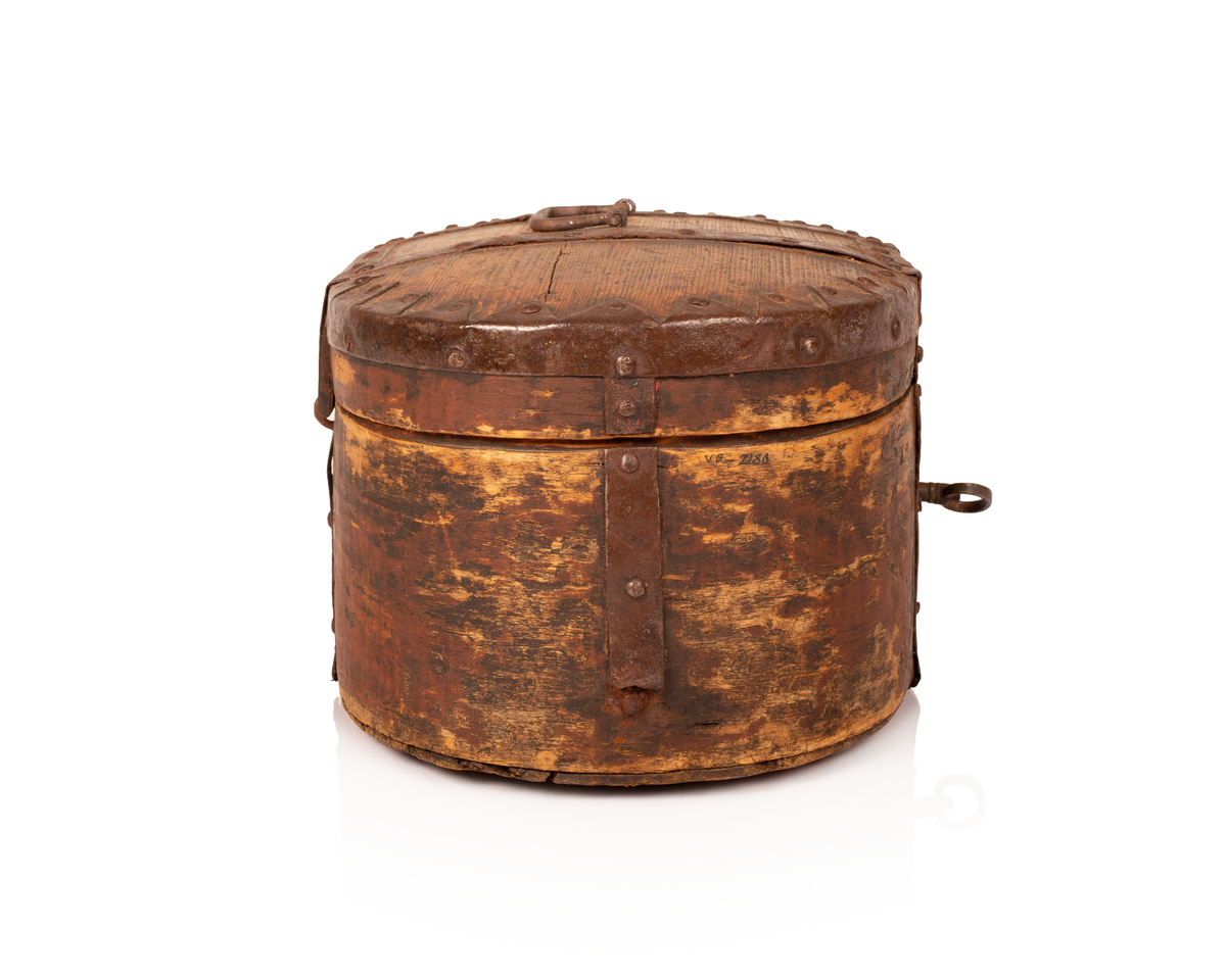 Brun bomme med lås og nøkkel. Den er ovalformet med et svakt hvelvet lokk som er festet med hengsler. Bunnen av bommen er plan. Videre er både bunnen av bommen og toppen av lokket laget av gran, mens sidene er laget av bjørk. 

Lokket og bommens sider er sveipet og består av tynne bjørkelapper, i relativ kraftige dimensjoner, som er brettet sammen for å danne bommens form. Bjørkelappen overlapper hverandre med en god del cm på baksiden og er festet med dobbel nagling. Det er fire nagler i hver av de to rekkene som fester siden sammen. De to rekkene står parallelle overfor hverandre med ca. 5 cm mellomrom. Siden til lokket er festet med en nagle i hver rekke, og i tillegg er det satt inn en nagle nederst på bommen mellom de to rekkene samt en i lokket. 

To smidde jernbånd går fra fremsiden av bommen over lokket og ned på baksiden. På baksiden er det satt inn løkkehengsler i jernbåndene til lokket. Båndene er satt på plass med jernnagler. Rundt toppen av lokket er det et jernbånd som fester lokkets topp og side sammen. Båndet er bøyd over siden, festet med nagler og dekorerte med innovervendte tagger. Midt på bommens lokk er det et håndtak som er festet med nagler. Det er i tillegg jernbånd som går ned på hver side av bommen, disse strekker seg ikke over lokket. 

Bommen har en smidd lås med et hjerteformet nøkkelskilt, og en tilhørende nøkkel. Man kan se rester av brun oljemaling på utsiden av bommen. 