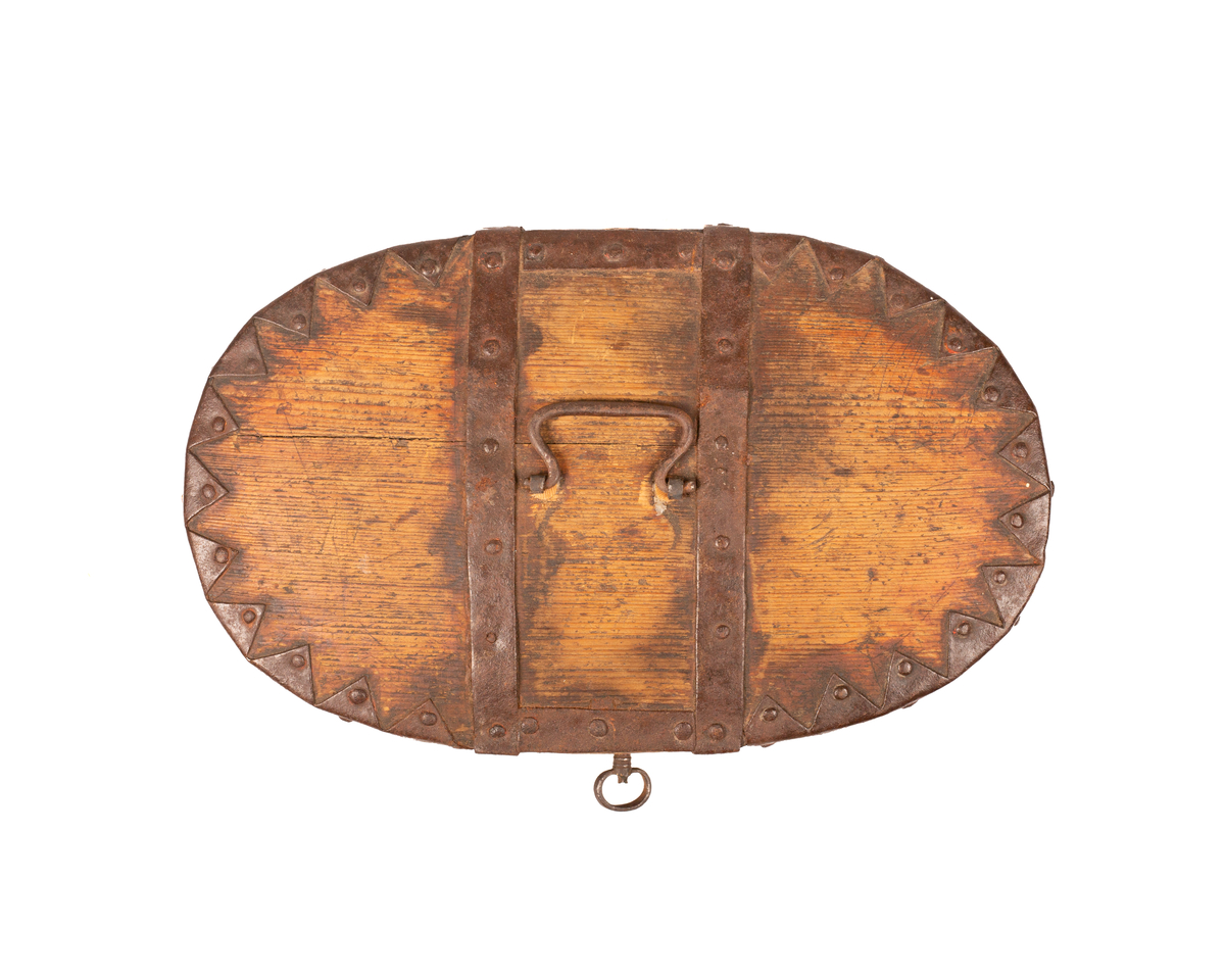 Brun bomme med lås og nøkkel. Den er ovalformet med et svakt hvelvet lokk som er festet med hengsler. Bunnen av bommen er plan. Videre er både bunnen av bommen og toppen av lokket laget av gran, mens sidene er laget av bjørk. 

Lokket og bommens sider er sveipet og består av tynne bjørkelapper, i relativ kraftige dimensjoner, som er brettet sammen for å danne bommens form. Bjørkelappen overlapper hverandre med en god del cm på baksiden og er festet med dobbel nagling. Det er fire nagler i hver av de to rekkene som fester siden sammen. De to rekkene står parallelle overfor hverandre med ca. 5 cm mellomrom. Siden til lokket er festet med en nagle i hver rekke, og i tillegg er det satt inn en nagle nederst på bommen mellom de to rekkene samt en i lokket. 

To smidde jernbånd går fra fremsiden av bommen over lokket og ned på baksiden. På baksiden er det satt inn løkkehengsler i jernbåndene til lokket. Båndene er satt på plass med jernnagler. Rundt toppen av lokket er det et jernbånd som fester lokkets topp og side sammen. Båndet er bøyd over siden, festet med nagler og dekorerte med innovervendte tagger. Midt på bommens lokk er det et håndtak som er festet med nagler. Det er i tillegg jernbånd som går ned på hver side av bommen, disse strekker seg ikke over lokket. 

Bommen har en smidd lås med et hjerteformet nøkkelskilt, og en tilhørende nøkkel. Man kan se rester av brun oljemaling på utsiden av bommen. 